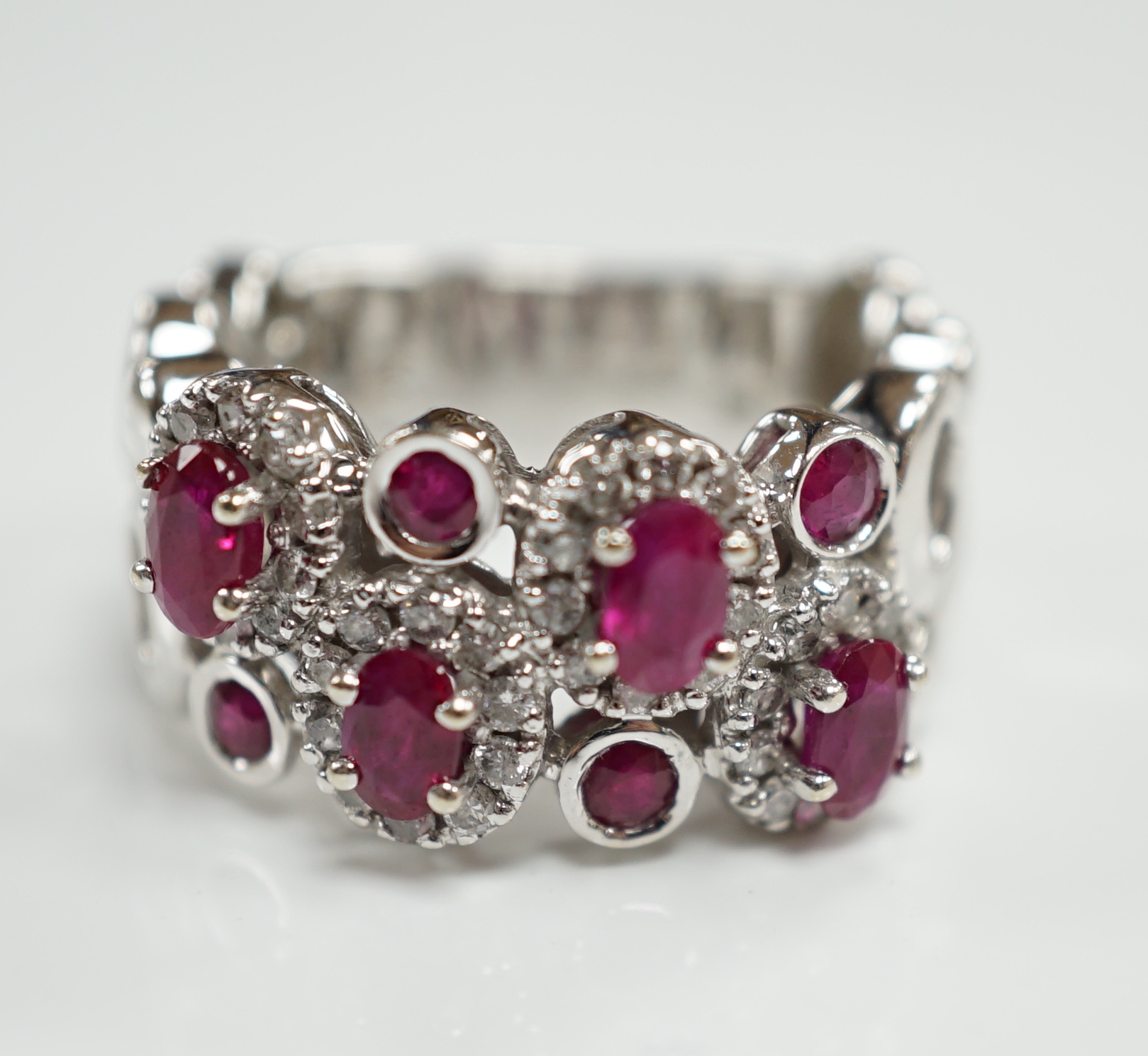 A modern 14ct white gold, ruby and diamond set multi cluster half hoop dress ring, size O, gross weight 8.1 grams.